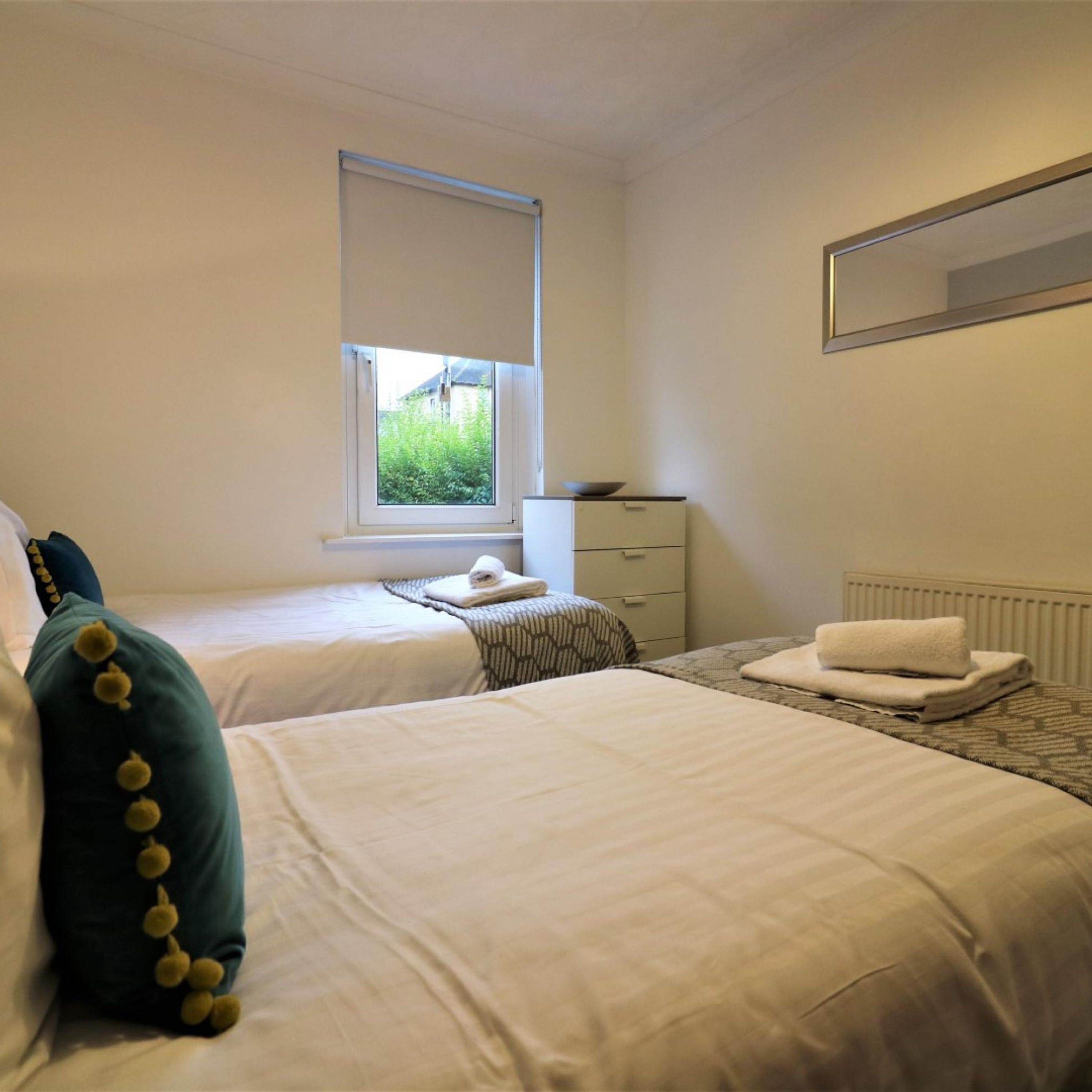 A bedroom with two beds, a window, a radiator, and a dresser.