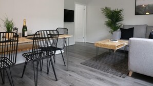 A modern living room with a grey sofa, a wooden coffee table, and a dining area with a wooden table and black chairs. - Caldercruix House - Airdrie (Airdrie)