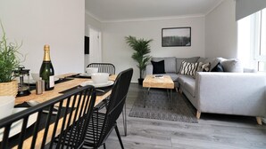 A modern living room with a grey sofa, a wooden dining table with chairs, a coffee table, and a large potted plant. - Caldercruix House - Airdrie (Airdrie)
