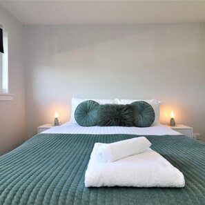 A neatly made bed with a green quilt, two white pillows, and a fluffy green accent pillow. There are two bedside lamps and a white nightstand. - Morland House - East Kilbride (Glasgow)