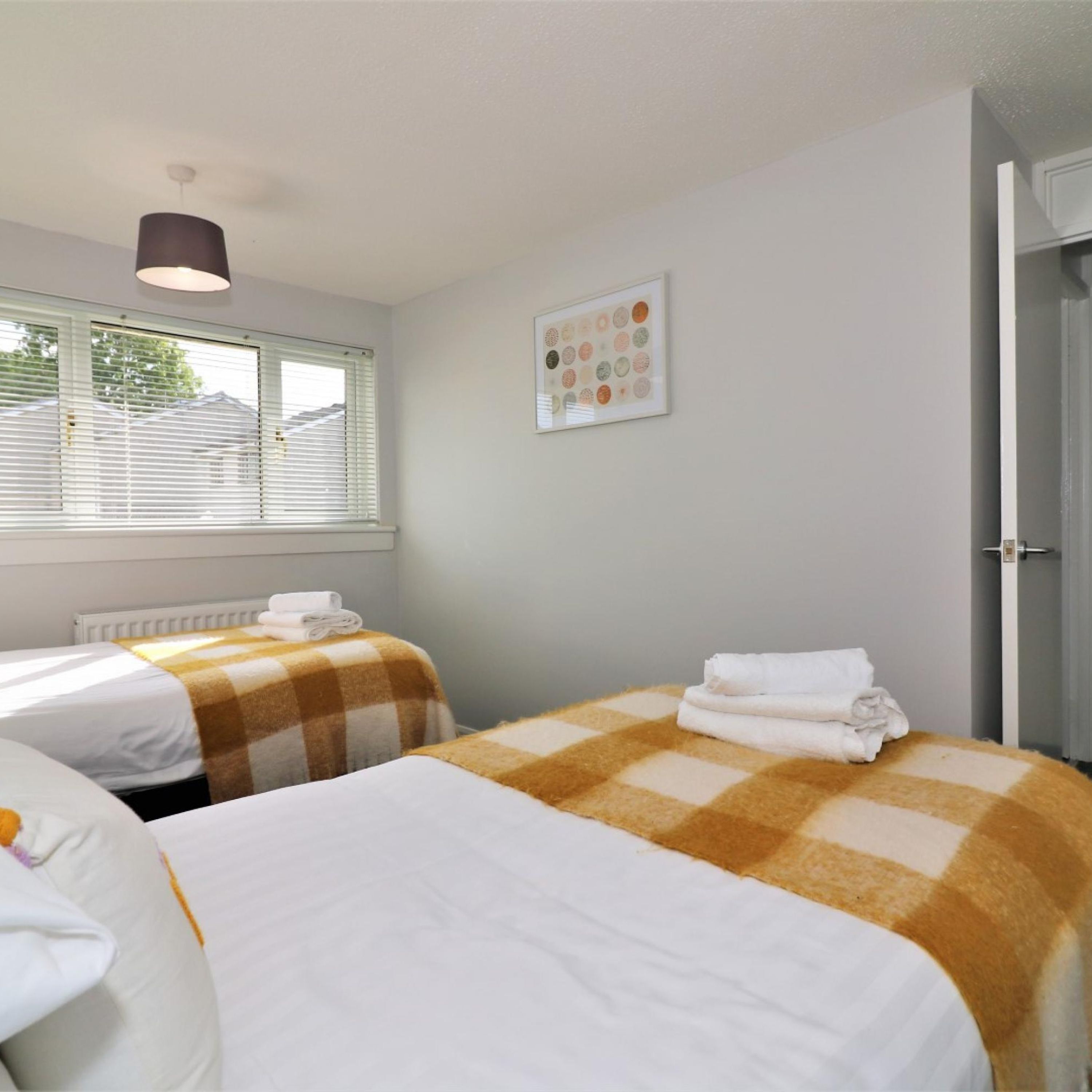 A hotel room with two beds, a radiator, a window with blinds, a ceiling light, and a framed picture on the wall.