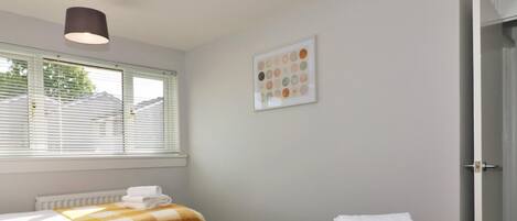 A hotel room with two beds, a radiator, a window with blinds, a ceiling light, and a framed picture on the wall.