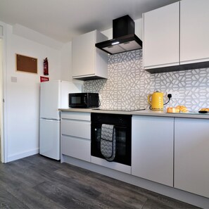 A modern kitchen with white cabinetry, a black microwave, a yellow kettle, and a patterned backsplash. - Morland House - East Kilbride (Glasgow)