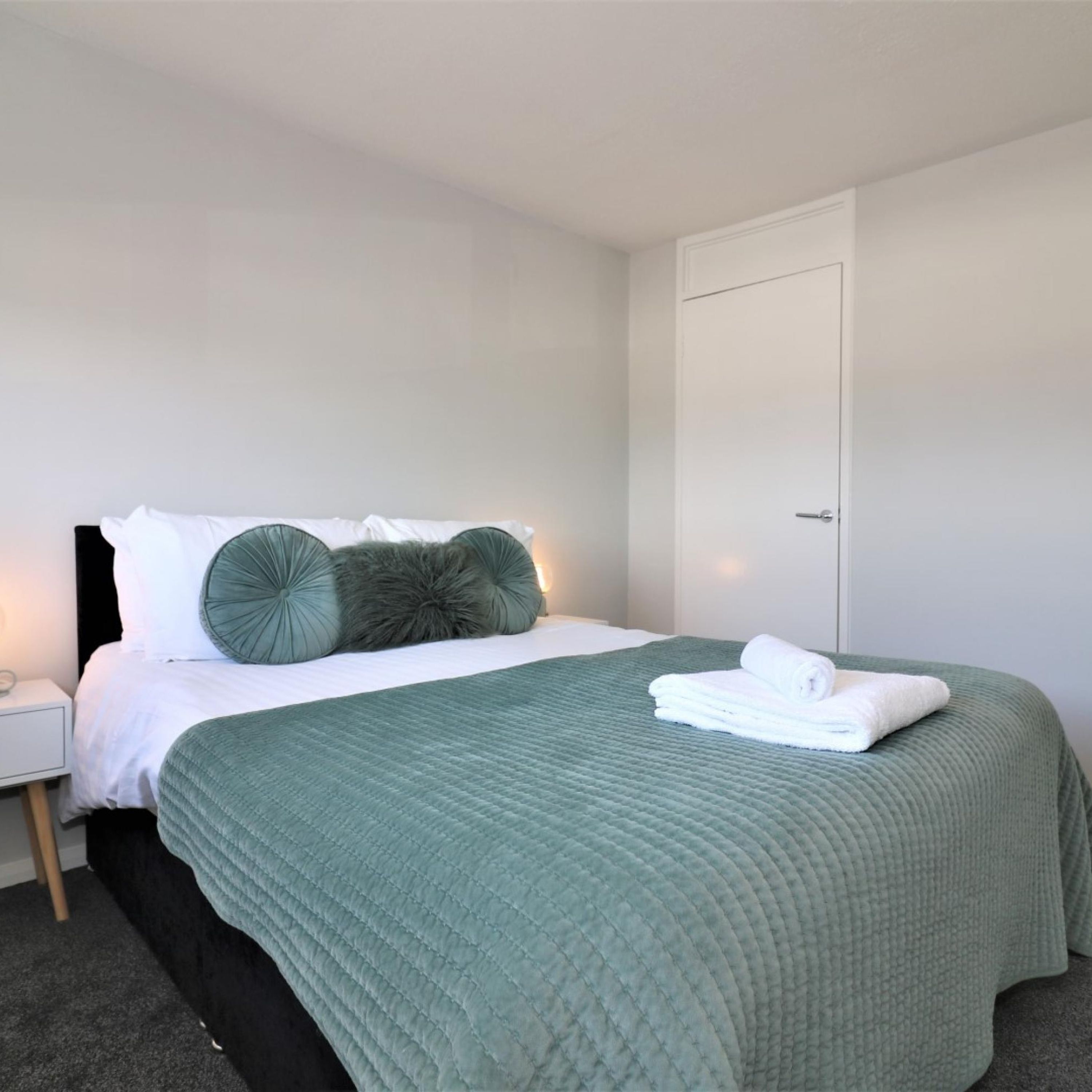 A neatly made bed with a green quilt, white linens, and decorative pillows.