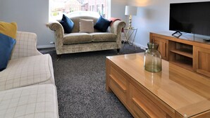 Een woonkamer met een bank, een salontafel, een televisie en een lamp.