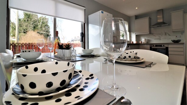 Een moderne keuken met een eettafel gedekt voor twee personen, met zwart-wit stipplatten en een wijnglas.