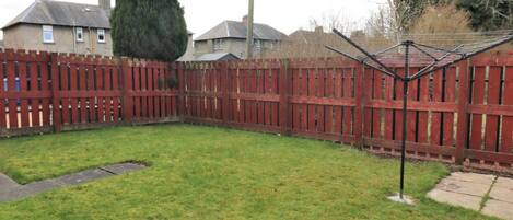 A fenced backyard with a grassy lawn and a clothes drying rack.