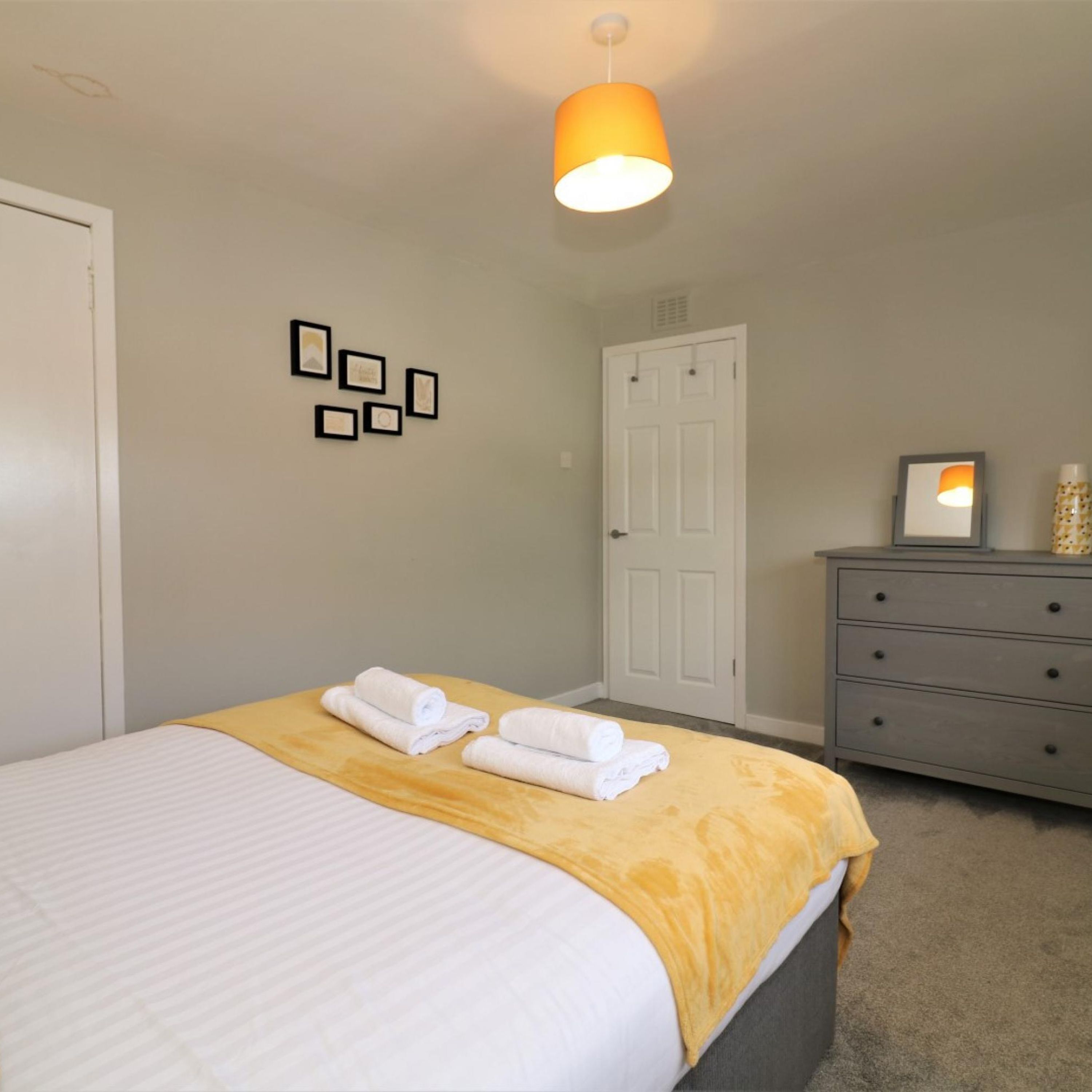 Ein Schlafzimmer mit Bett, Kommode, Tür und Wandbildern.