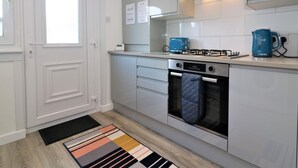 Une cuisine moderne avec des meubles blancs, une cuisinière à gaz, une bouilloire bleue et une fenêtre donnant sur un beau paysage.