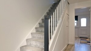 Un escalier avec des marches en pierre et des rampes noires, menant à un palier doté d’une porte.