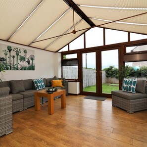A spacious living area with a large window, a sofa set, a wooden coffee table, and a ceiling fan. - Barons Court - Paisley (Paisley)