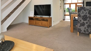 Una sala moderna con un mueble de televisión de madera, una zona de comedor con una silla estampada, y una escalera.