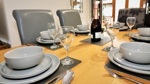 Una mesa de comedor dispuesta con platos, tazones, copas de vino y cubiertos.