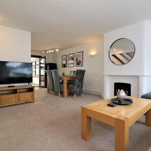 A modern living room with a TV, dining table, and chairs. There is a fireplace and a mirror on the wall. - Barons Court - Paisley (Paisley)