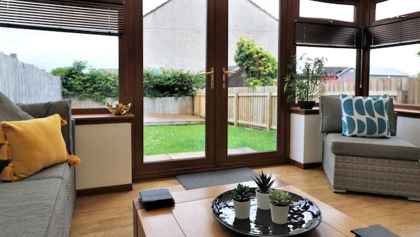 Un solárium con vistas a un jardín trasero, un sofá gris, una mesa de centro con plantas y una silla de mimbre.