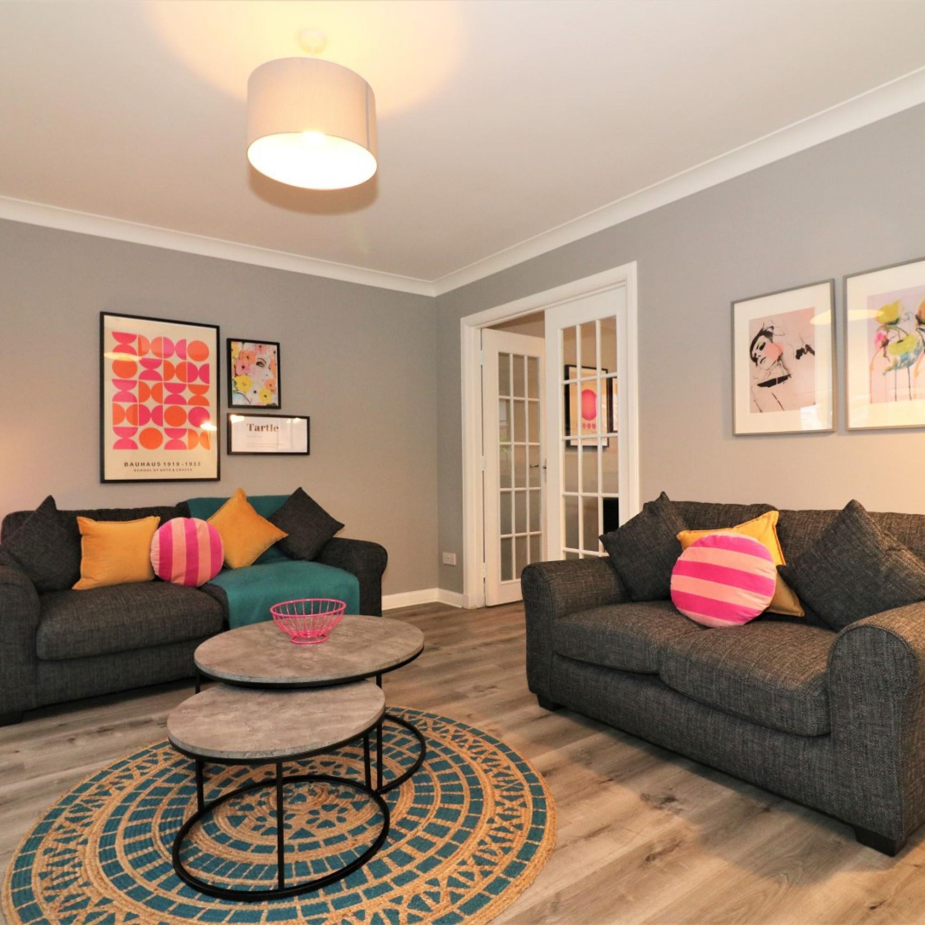 A living room with two grey sofas, colorful cushions, a round coffee table, and a patterned rug.