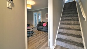 A hallway with a carpeted staircase, a dining area with a round table and chairs, and a gray sofa with a pink pillow. - Carnbroe House - Carnbroe (Coatbridge)