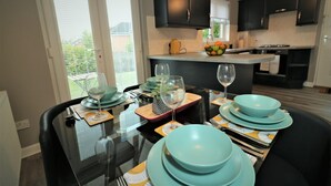 A modern kitchen with black cabinets, a dining table set with teal plates and wine glasses, and a view of the outside through a window. - Carnbroe House - Carnbroe (Coatbridge)