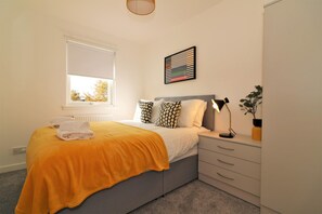 A bedroom with a bed, a bedside table with a lamp, a window with blinds, a radiator, and a wall-mounted artwork. - Great Western View - Glasgow (Glasgow)