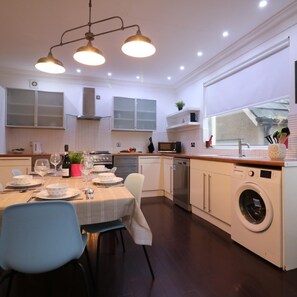 A modern kitchen with a dining area, a washing machine, and a window overlooking the garden.