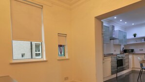 Une cuisine moderne avec des meubles blancs, un four encastré et un four à micro-ondes. On y trouve une fenêtre avec des stores et une petite fenêtre décorative avec des vitraux.