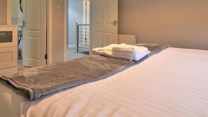 Une chambre avec un grand lit, une porte menant à la salle de bain et un couloir qui donne sur une autre pièce.