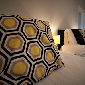 A hotel room with a neatly made bed, a patterned throw pillow, and a bedside lamp.