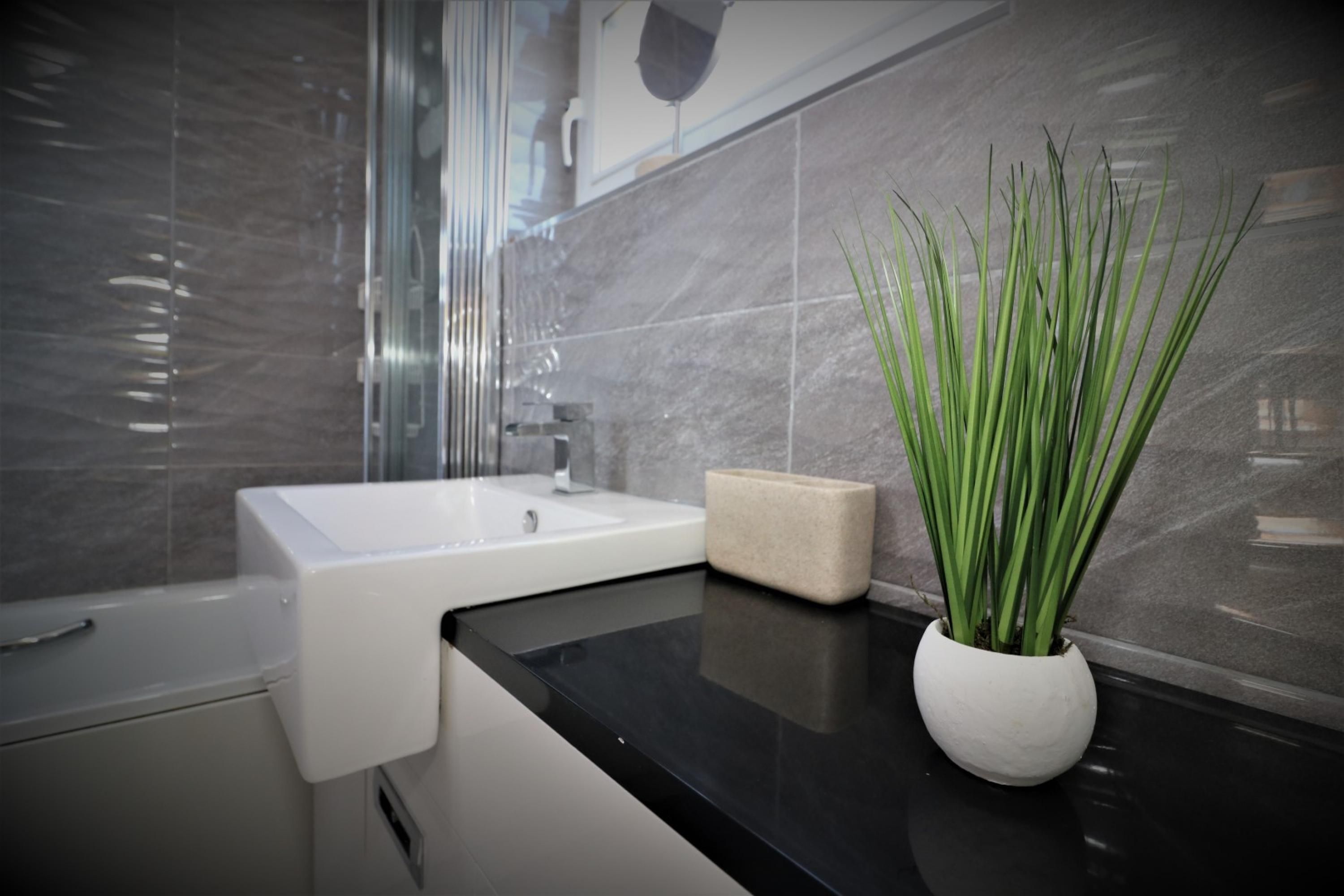 A modern bathroom with a white sink, a beige soap dish, and a white vase with green plants.
