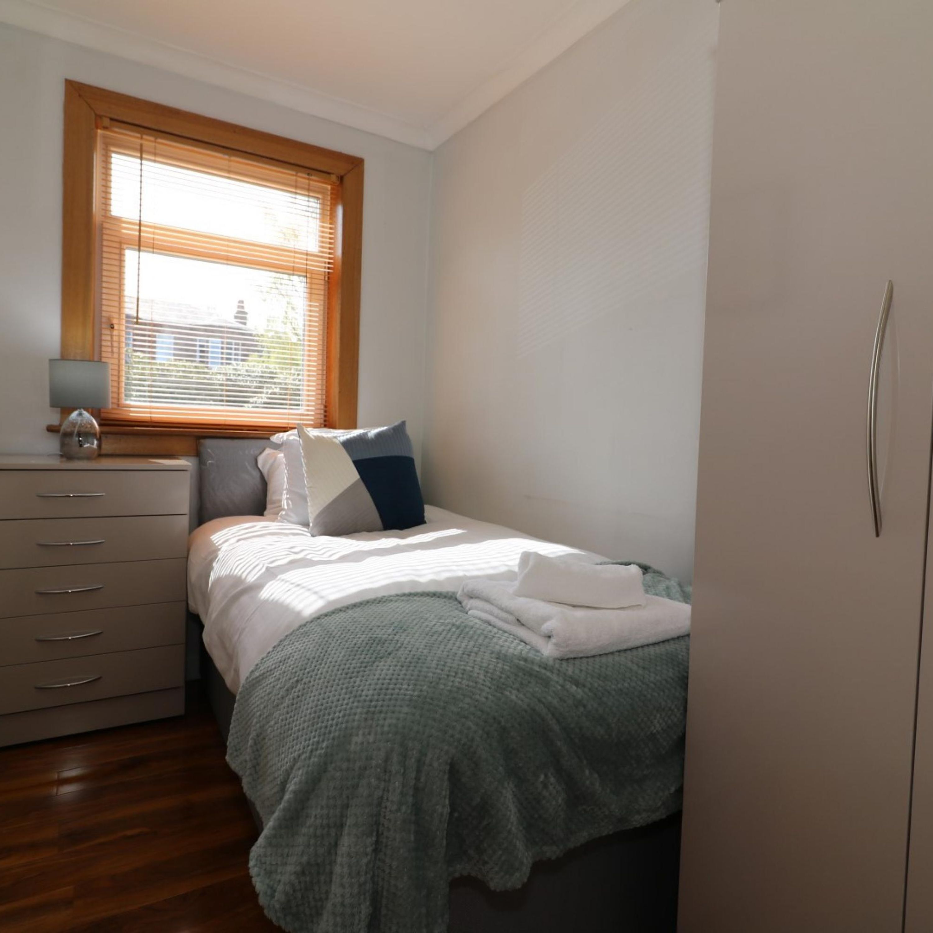 Un dormitorio con cama, cómoda, ventana con persianas y armario.