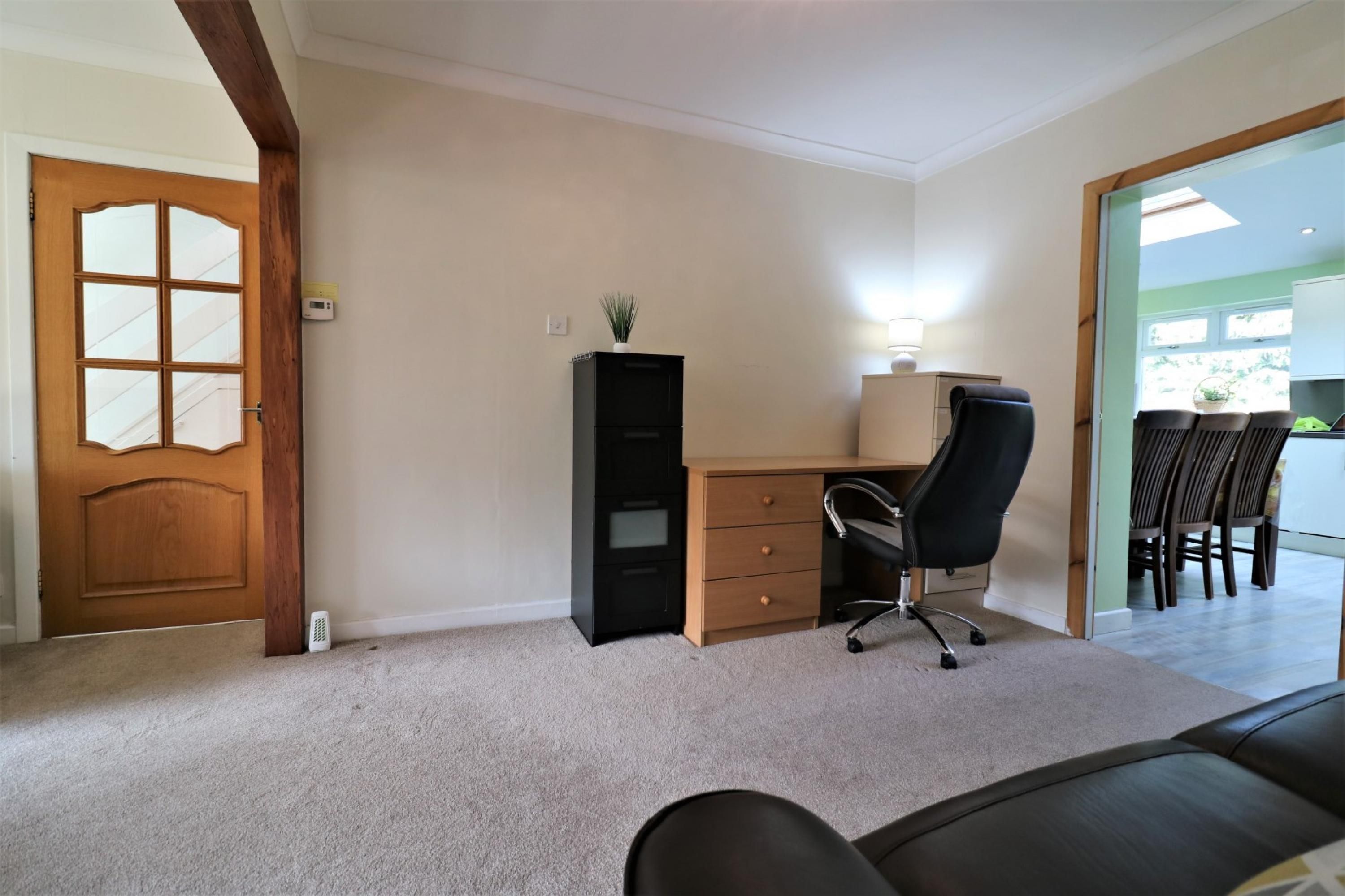 A room with a wooden door, a desk with a chair, a small plant, and a dining area with chairs.
