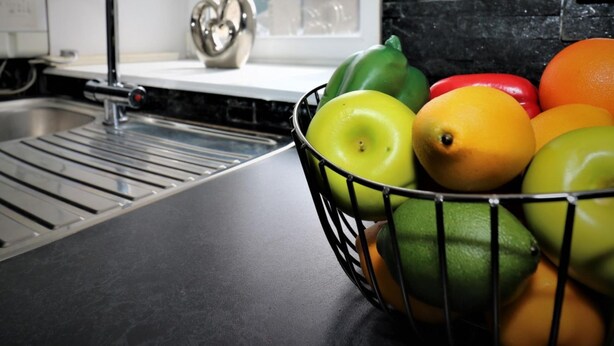 A kitchen with a black countertop, a stainless steel sink, and a fruit bowl containing apples and oranges. - Kirkhill Middle - Lanark (Lanark)