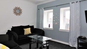 A modern living room with a black sofa, a glass coffee table, and a decorative mirror on the wall. - Kirkhill Middle - Lanark (Lanark)