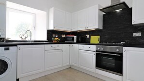 A modern kitchen with white cabinets, a black backsplash, a microwave, a stove, and a washing machine. - Kirkhill Middle - Lanark (Lanark)