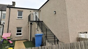 A residential building with a staircase leading to a second floor, a small outdoor seating area with a table and chairs, and a blue trash bin. - Kirkhill Middle - Lanark (Lanark)