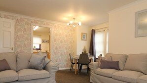 A living room with two sofas, a dining table with chairs, and a kitchen in the background. - Douglas View Blantyre (Glasgow)
