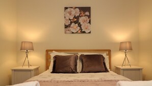A bedroom with a bed, two bedside lamps, a floral painting on the wall, and two towels on the bed. - Douglas View Blantyre (Glasgow)