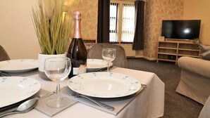 A dining area with a table set for two, a bottle of champagne, and a vase of pampas grass. - Douglas View Blantyre (Glasgow)