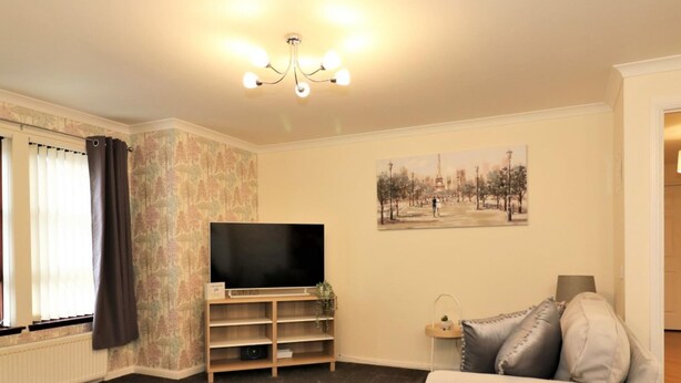 A living room with a flat-screen TV, a sofa, a chair, and a painting on the wall. - Douglas View Blantyre (Glasgow)