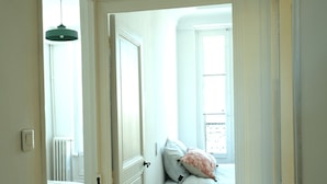 Un couloir étroit mène à une chambre à coucher qui contient un lit, une table de chevet et une fenêtre.