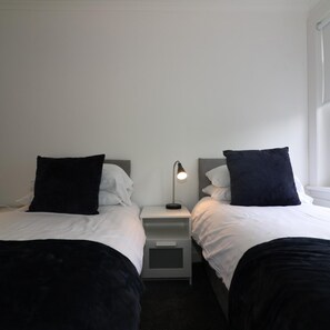 A twin room with two beds, a nightstand with a lamp, and a window. - New View House Bellshill (Bellshill)
