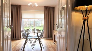 A dining area with a table set for four, a chandelier, and a view of a backyard through large windows. - Morrison House Holytown (Motherwell)