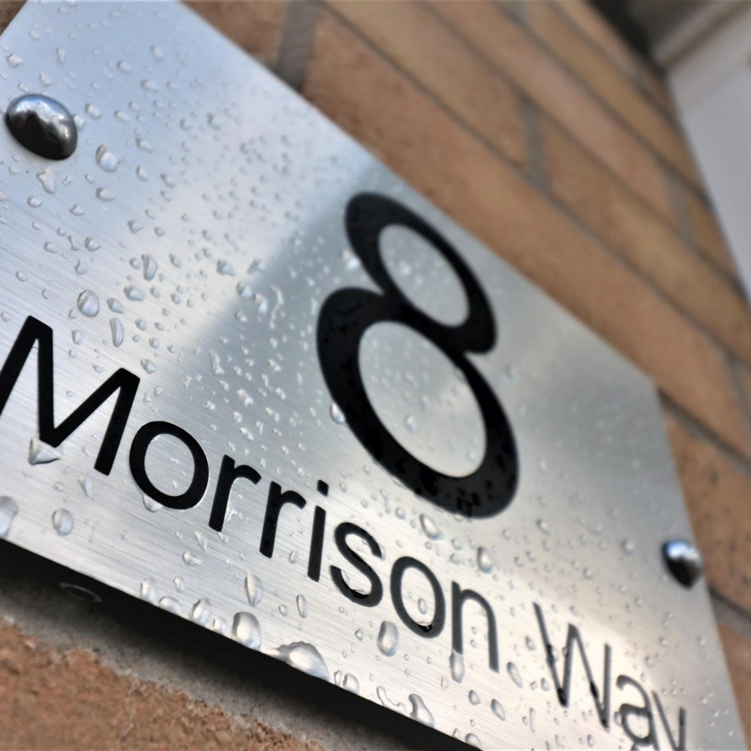 A metallic house number plaque with water droplets, indicating recent rain.