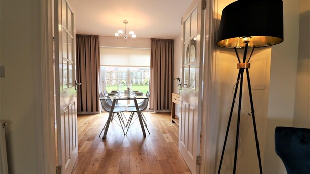 A room with a dining table and chairs, a floor lamp, and a view of a garden through a window. - Morrison House Holytown (Motherwell)