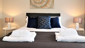 A hotel room with a large bed, two nightstands, a wall-mounted abstract painting, and two white towels on the bed. - Morrison House Holytown (Motherwell)