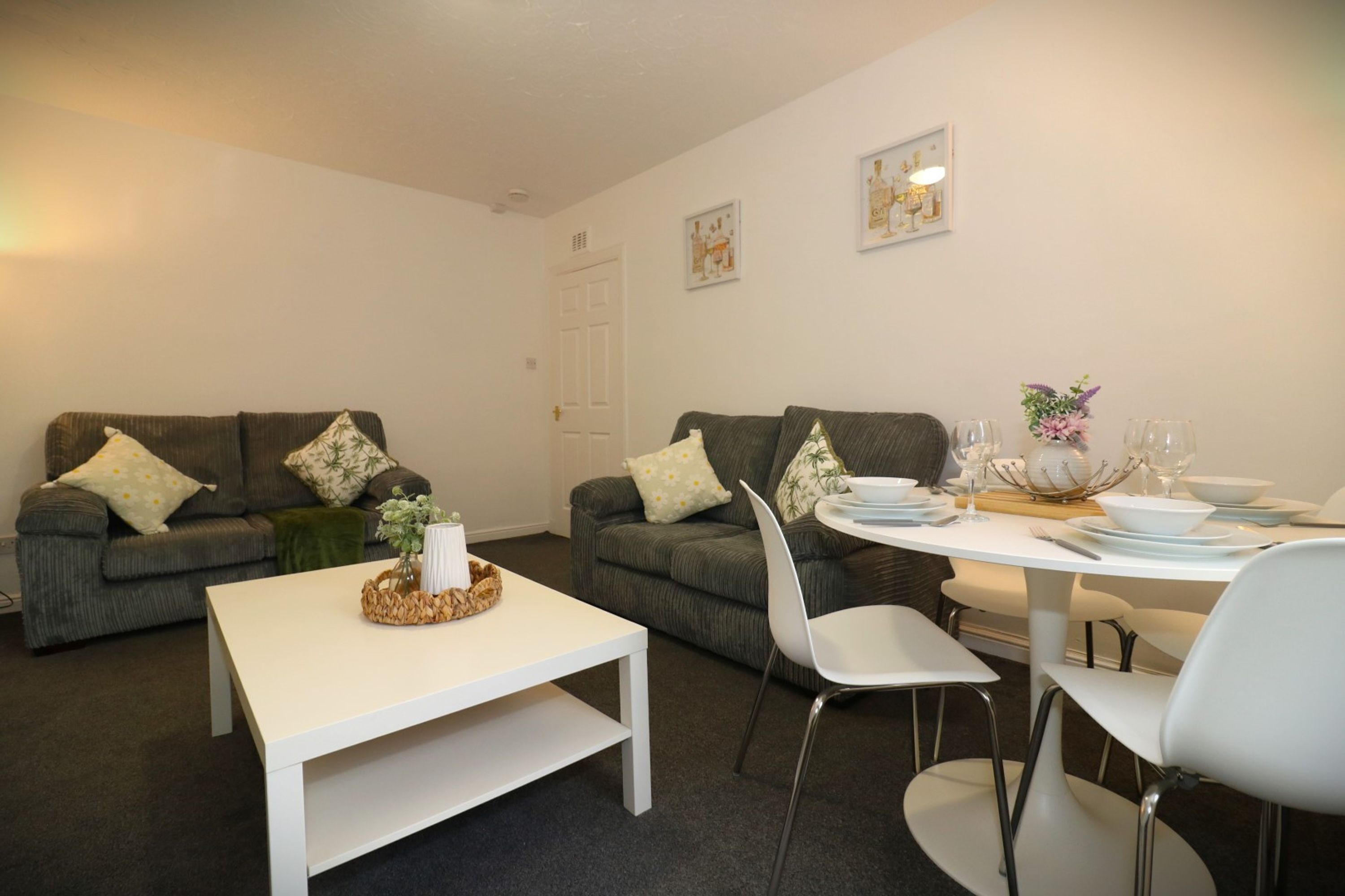 A modern living room with two grey sofas, a white coffee table, and a dining table set for four.