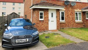 A two-story residential building with a brick facade, a white door, and satellite dishes on the roof.