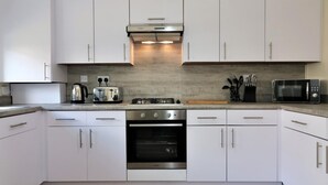 A modern kitchen with white cabinets, a gas stove, an oven, a microwave, and a hanging light fixture.