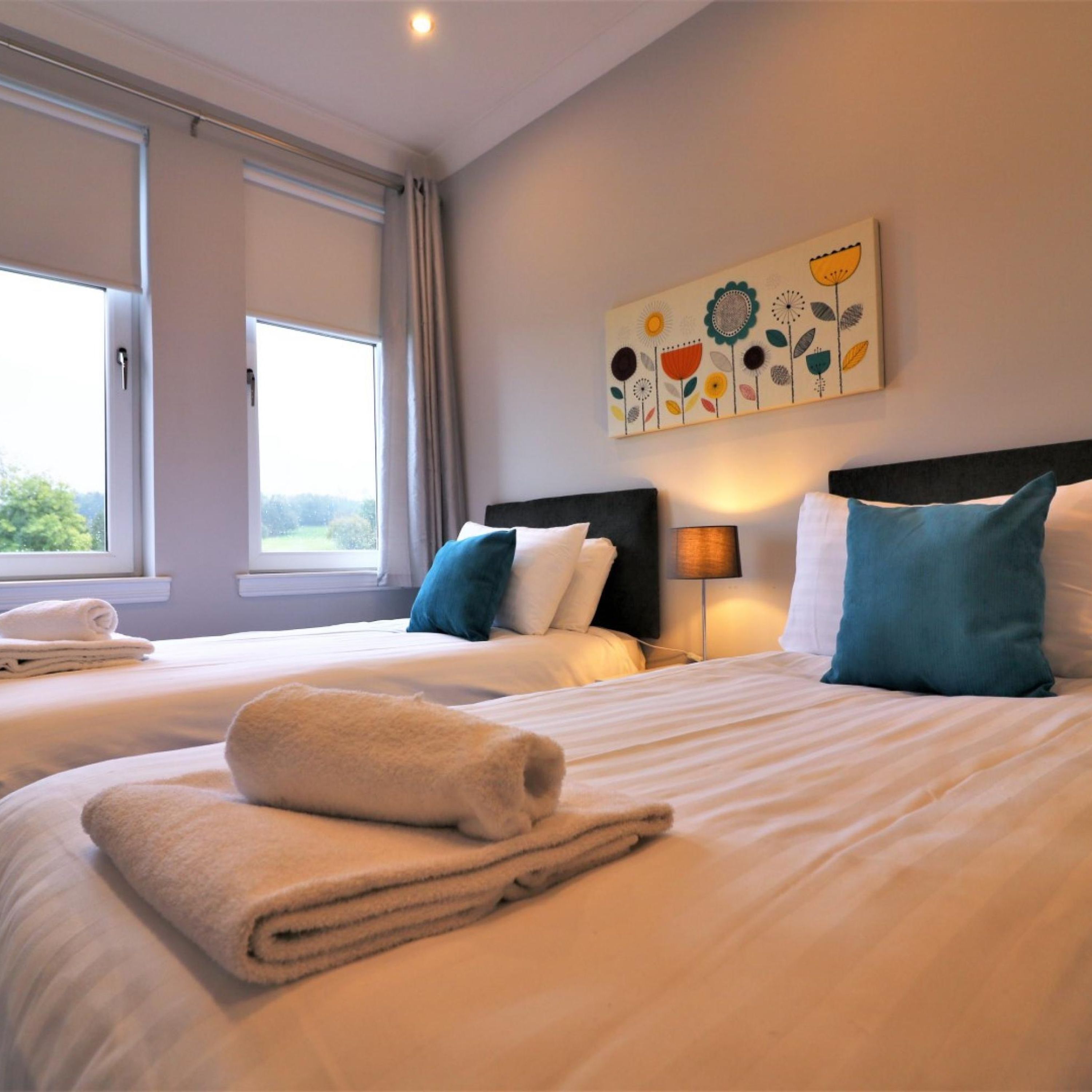 A hotel room with two beds, a large window, and a floral artwork on the wall.