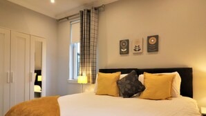 Een slaapkamer met een groot bed, een kledingkast, een raam met gordijnen en wanddecoratie.