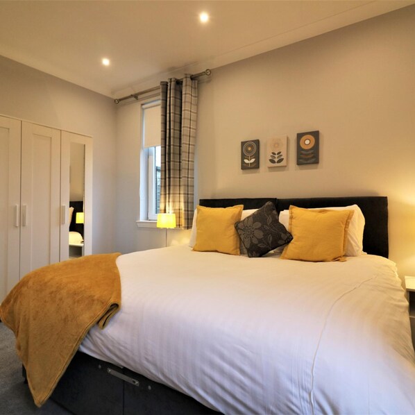 A bedroom with a large bed, a wardrobe, a window with curtains, and wall art.